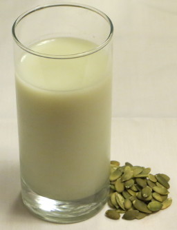 glass os pumpkin seed milk with seeds by its side